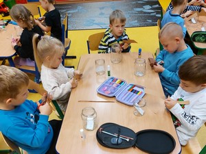 Dzieci z oddziału przedszkolnego (zerówka 02) siedzą przy stoliku i wykonują prace plastyczne.