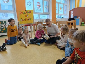 Dzieci z oddziału przedszkolnego (4 - latki) siedzą na podłodze i słuchają jak rodzic dziecka p. Iwetta czyta książkę.