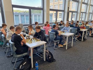 Uczestnicy Wojewódzkiego Turnieju Szachowego z okazji 100 lecia Kartuz siedzą przy stolikach i grają w szachy.