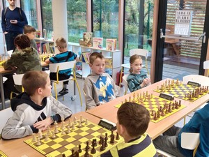 Szachiści uczestniczący w IX Mistrzostwach Dzielnicy Gdyni Mały Kack w Szachach siedzą przy stolikach i grają w szachy.