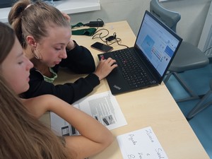 Uczennice biorące udział w projekcie mPotęga siedzą przy stoliku i projektują na laptopie breloczek.