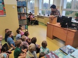 Dzieci z oddziału przedszkolnego (5 - latki) siedzą na podłodze i słuchaja pani bibliotekarki.