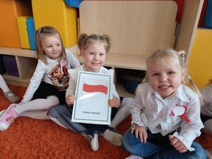 Dzieci z oddziału przedszkolnego (4 - latki) siedzą na dywanie i prezentują flagę Polski.