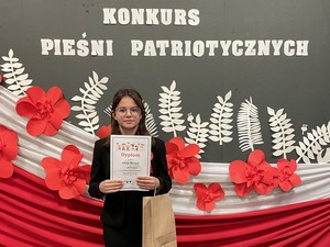 Uczennica Alicja Marszk (7b) prezentuje się do zdjęcia podczas VII Powiatowego Konkursu Pieśni Patriotycznej w Baninie.
