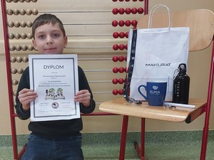 Uczeń Franciszek Zaborowski (1b) prezentuje się do zdjęcia z dyplomem i nagrodą jaką otrzymał w Powiatowym Konkursie Plastycznym "Bezpieczna droga – znam zasady ruchu drogowego".