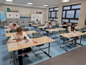 Uczniowie z klas 8 siedzą przy stolikach i piszą próbny egzamin ósmoklasisty.