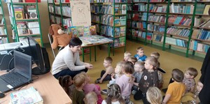 Dzieci z oddziału przedszkolnego (3 - latki) siedzą na podłodze Biblioteki Szkolnej i słuchają p. Moniki Młyńskiej – szkolnej bibliotekarki.
