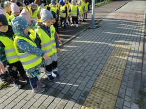Dzieci z oddziału przedszkolnego (5 - latki) stoją przed znakami dla osób niewidomych na chodniku.