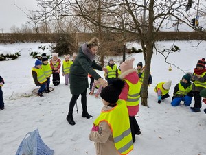 Dzieci z oddziału przedszkolnego (4 - latki) wraz z wychowawczynią stoją w parku i dokarmiają ptaki.