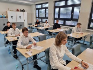 Uczniowie z klas ósmych siedzą przy stolikach i piszą próbny egzamin ósmoklasisty.