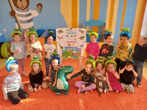 Dzieci z oddziału przedszkolnego (5 – latki) prezentują się do zdjęcia przy planszy wykonanej z okazji Dnia Dinozaura.