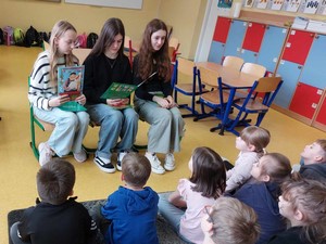 Trzy uczennice z klasy 7a siedzą i czytają bajki uczniom z oddziałów przedszkolnych.